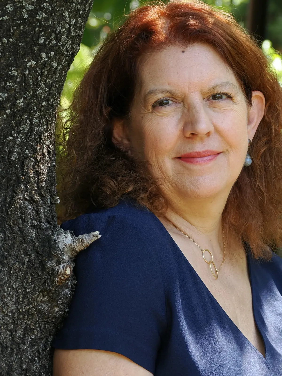 Christine nous regarde, appuyée contre un arbre